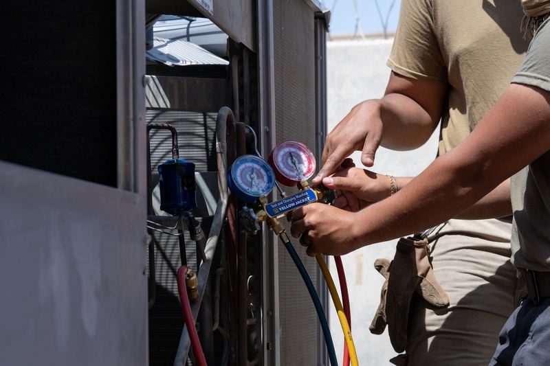 Heating, ventilation and air conditioning technicians assigned to the 379th Expeditionary Civil Engineer Squadron use a pressure gauge to inspect the condition of a newly repaired 